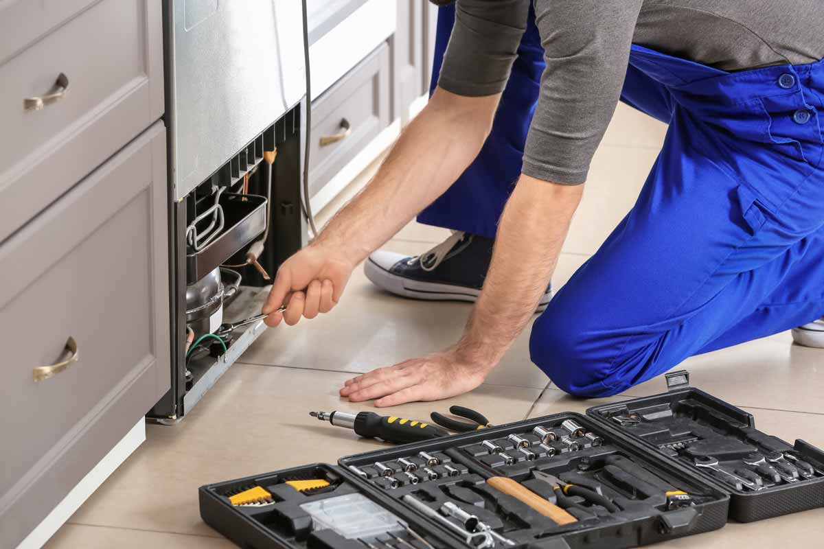 A man kneeling to repair a refrigerator