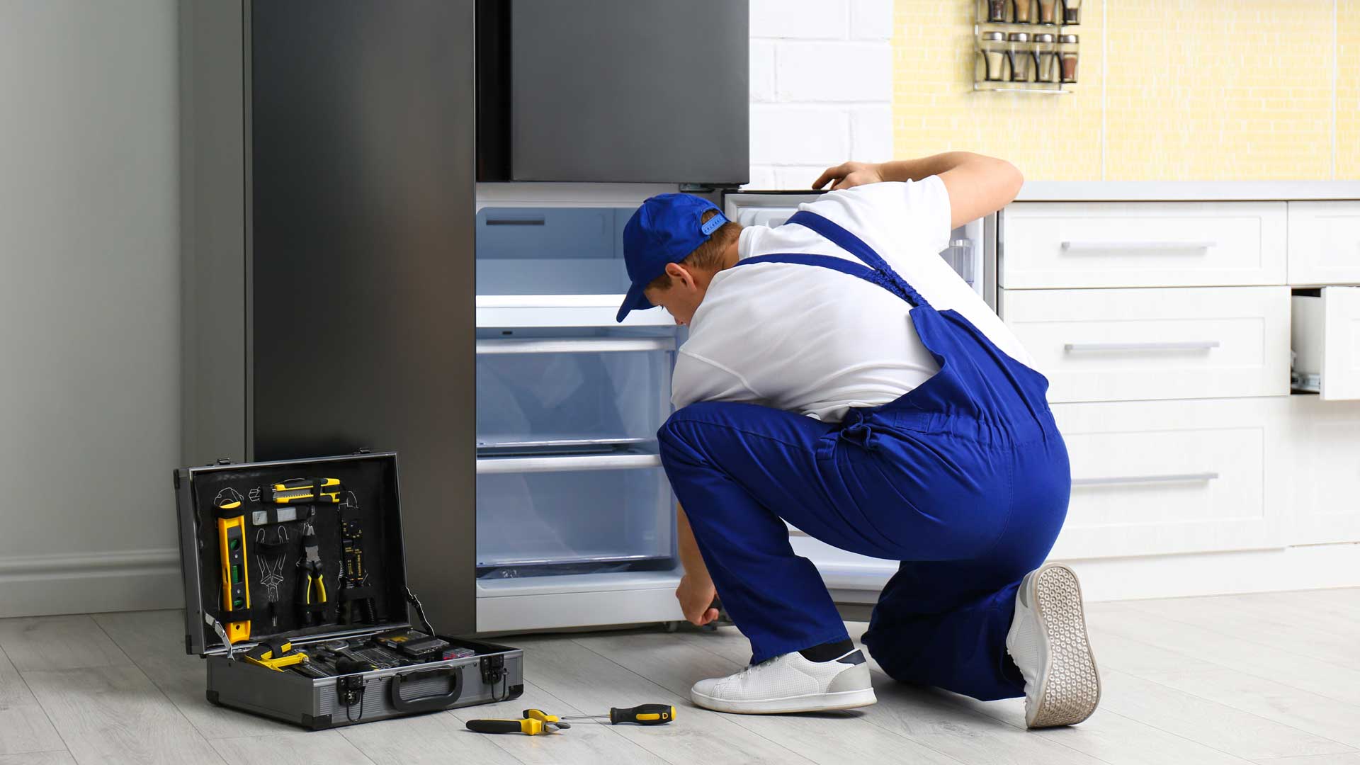 A technician in blue overalls repairing a refrigerator